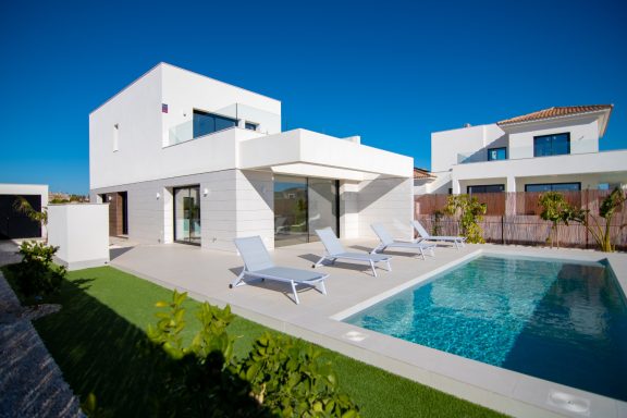 Maison moderne avec piscine, transats et pelouse, sous un ciel bleu.
