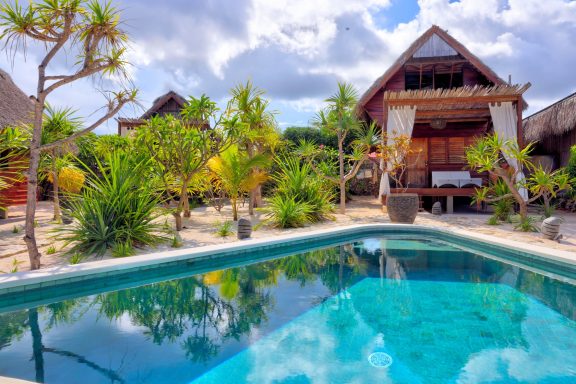 Villa avec piscine, jardin tropical, et ciel nuageux en arrière-plan.