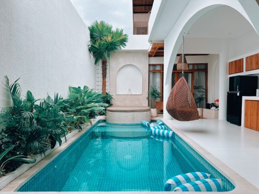 Piscine intérieure avec une balançoire, entourée de plantes tropicales et de murs blancs.