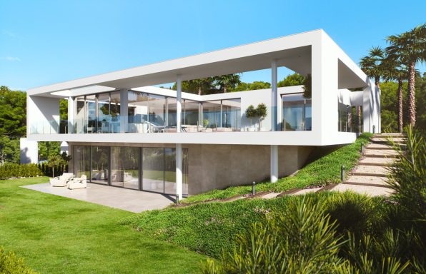 Maison moderne en béton avec balcons, située dans un jardin verdoyant.