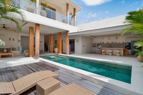 Villa moderne avec piscine, cuisine extérieure et espace détente sous un ciel ensoleillé.