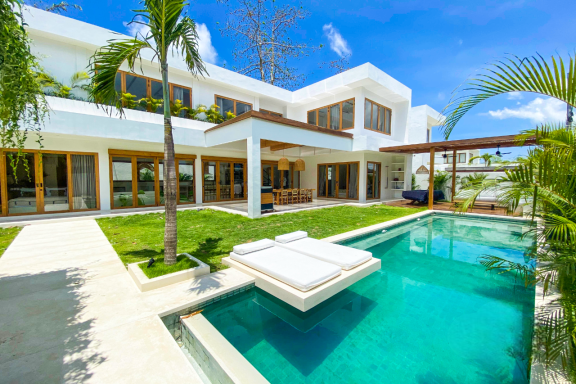 Maison moderne avec piscine, jardin verdoyant et ciel bleu dégagé.