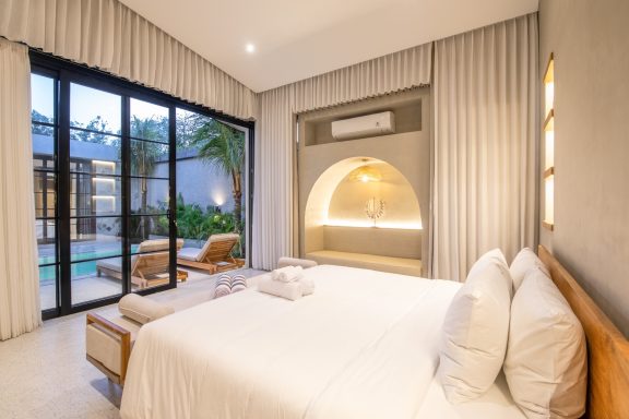 Chambre moderne et lumineuse avec lit double, vue sur une terrasse et piscine.